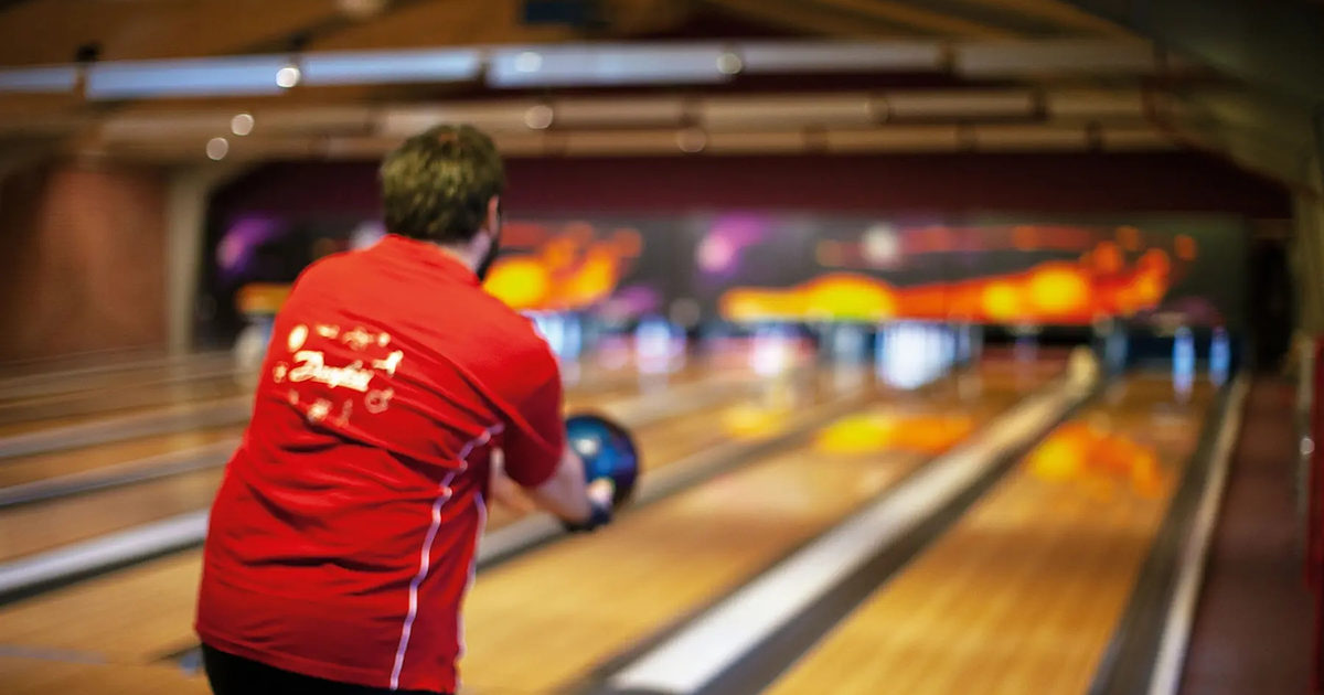 Bowlingspiller i rød trøje sender kuglen af sted i Kuglen og Keglen