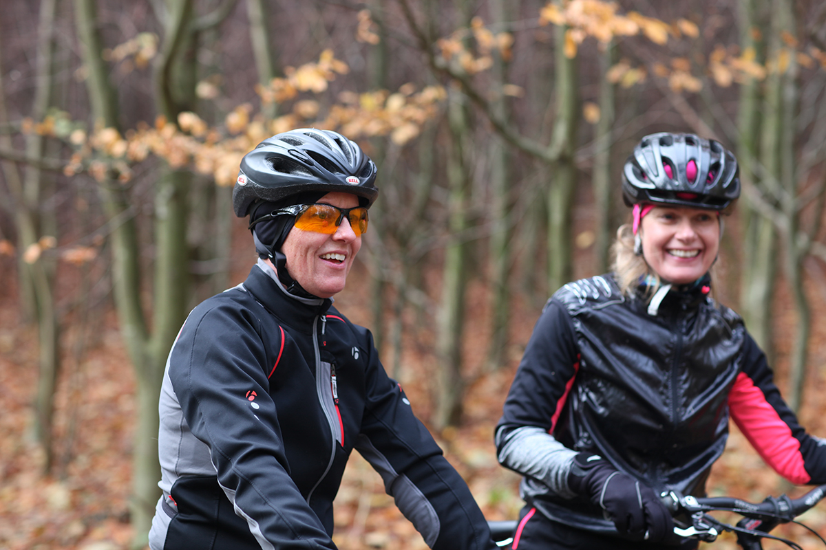 To cyklister i hjelm og vinterjakke på tur gennem skoven en efterårsdag